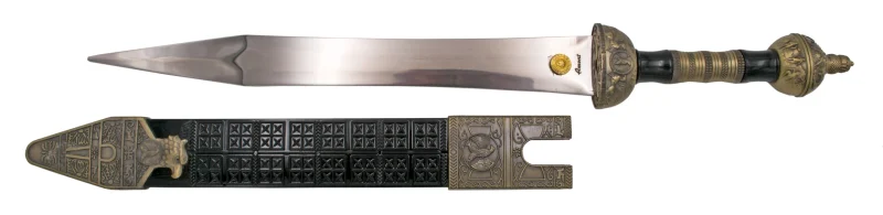Daga Romana S3327, el pomo está acabado en bronce antiguo y el mango en plástico negro con parte metálica en bronce antiguo, la guarda acabada en bronce antiguo. El tamaño total es de 46,5 cm con hoja de acero. La vaina está acabada en plástico negro con las partes metálicas en bronce antiguo. Ref. S3327