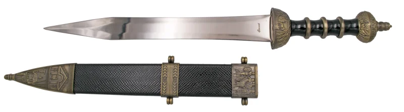 Daga Romana S3328, el pomo está acabado en bronce antiguo y el mango en plástico negro con aros metálicos en bronce antiguo, la guarda acabada en bronce antiguo. El tamaño total es de 46,5 cm con hoja de acero. La vaina está acabada en plástico negro con las partes metálicas en bronce antiguo. Ref. S3328